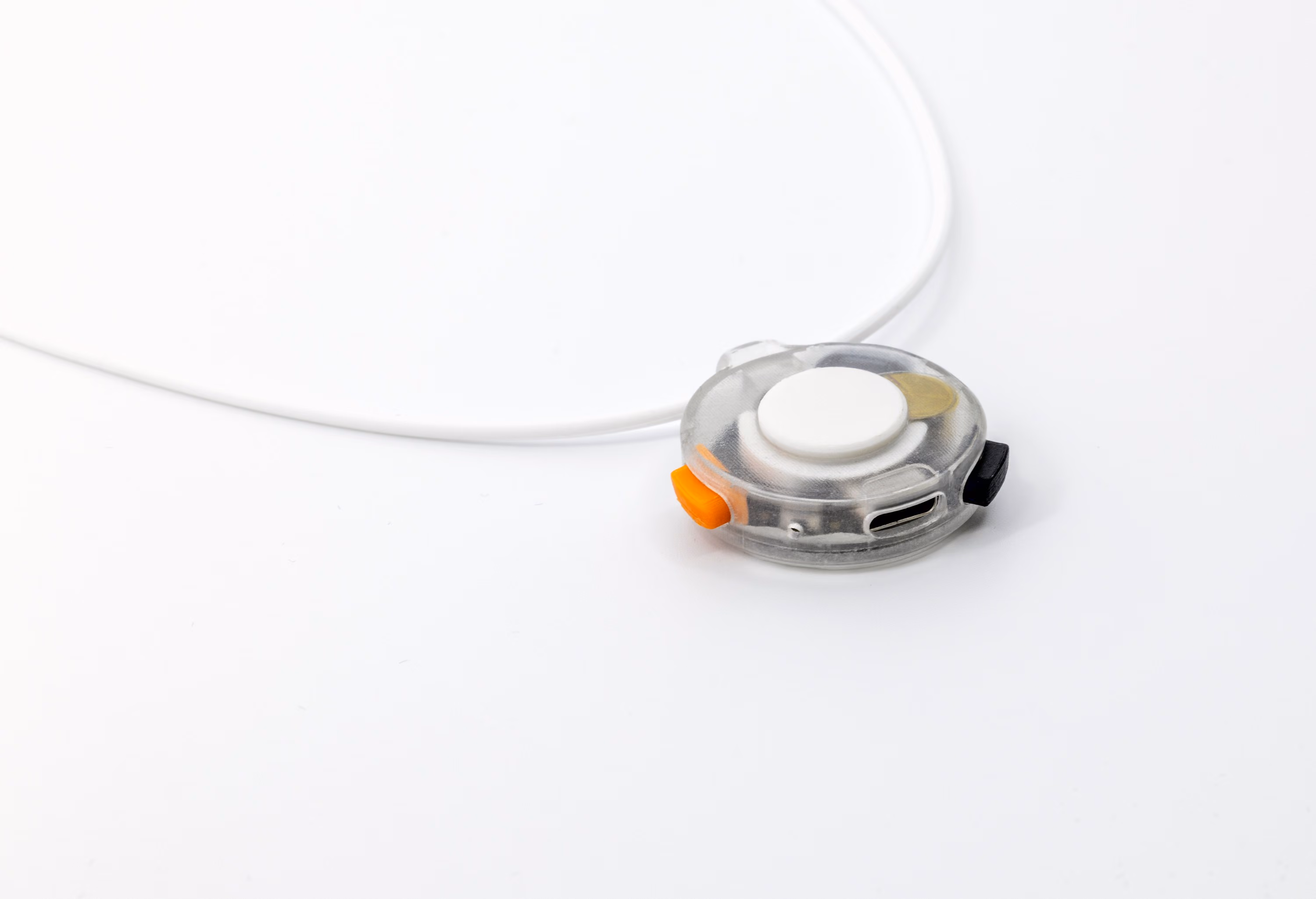 Close-up of VOX on its cord: the capture button on top, the orange and dark side controls, the skin-contact microphone, and the USB-C charging port along the edge.
